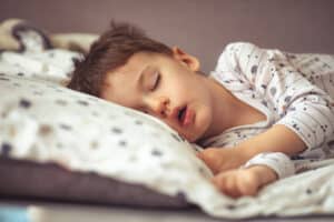 Peaceful child sleeping with mouth slightly open, illustrating symptoms of enlarged adenoids such as mouth breathing and disrupted sleep
