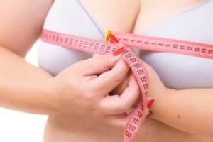 Close-up of a plus-size woman measuring her chest with a tape measure, highlighting considerations for breast reduction and bra fitting