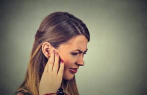 Woman holding her hand to her ear, showing discomfort or possible hearing or ear-related symptoms